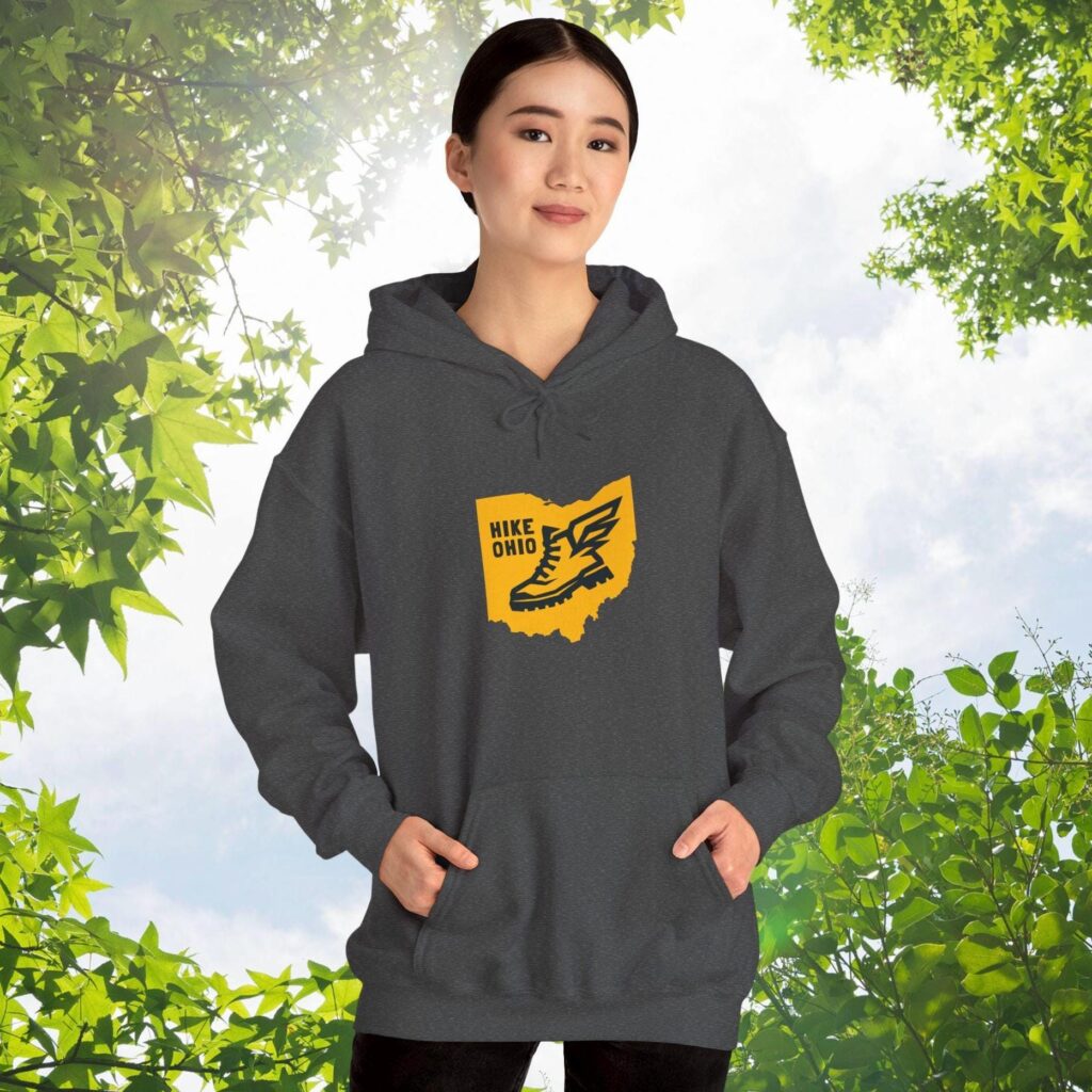 A woman is standing in a comfy hoodie with an orange state of Ohio graphic on it and the words "Hike Ohio"